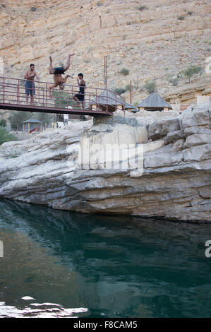 Man jumps from a bridge into the water at Wadi Bani Khalid, a natural canyon formation of rocks and crystal clear pools Stock Photo