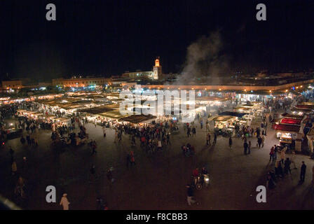 Main square Jemaa el-Fnaa in Marrakesh at night packed with food stalls, smoke rising over the lights, mosque in the background Stock Photo