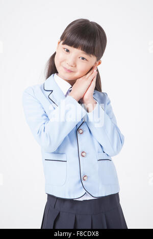 Elementary school girl in school uniforms with her hair in bunches putting her hands together close to her face and smiling Stock Photo