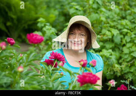 Happy mature woman in paeony plant at garden Stock Photo