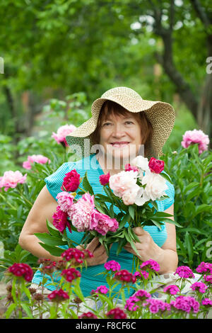 Happy mature woman in peony plant at garden Stock Photo