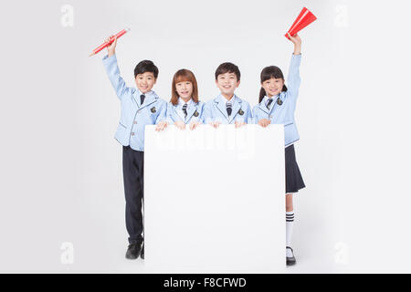White copy space on the floor and four elementary school students standing behind it and holding a big red pencil and a red Stock Photo