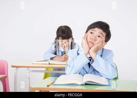 Elementary school boy in school uniforms seated at desk looking up with his hands cupped around his face with the background of Stock Photo
