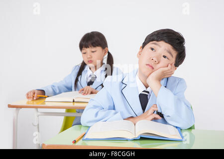 Elementary school boy in school uniforms seated at desk resting his chin on his hand with the background of a girl student Stock Photo