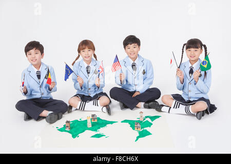 Four elementary school students sitting around a world map on the floor and holding flags each all staring forward with a smile Stock Photo