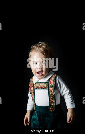 An 18 month old boy wearing lederhosen cries while he's sitting on a