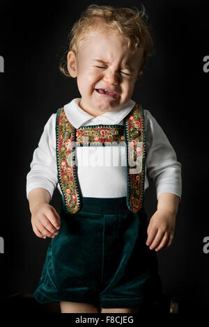 An 18 month old boy wearing lederhosen cries while he's sitting on a