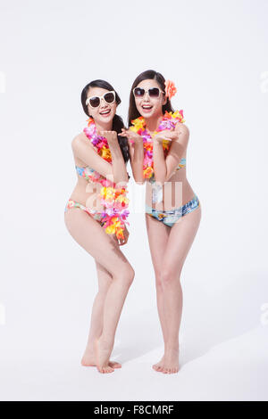 Two women in bikini and flower necklace wearing sunglasses standing together with their palms up close to their face and smiling Stock Photo