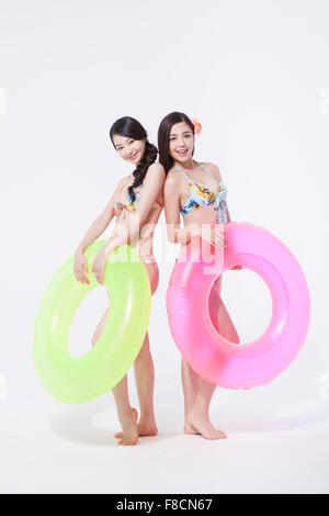 Two women in bikini standing back to back each other with a ring tube each both staring forward with a smile Stock Photo