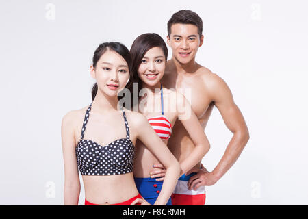 Two women in bikini and a man in swimming pants in a row with one hand on each waist staring forward with a smile Stock Photo