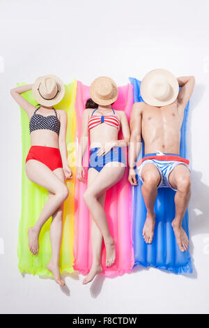 High angle of two women and a man in beach wear lying down on a float each with their faces covered with a hat each Stock Photo