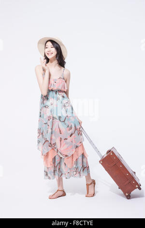 Woman in long dress and a hat carrying her suitcase and smiling Stock Photo