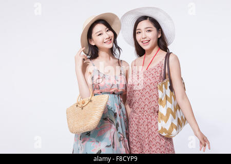 Two women in tourist fashion and a hat with a bag on close to each other staring forward with a smile Stock Photo