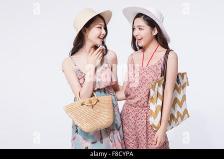 Two women in tourist fashion and a hat with a bag on close to each other looking at each other with a smile Stock Photo
