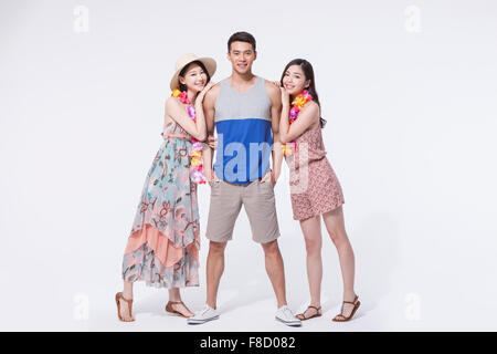 Two women in dress and flower necklaces standing and leaning on a man in casual outfit with his hands in his pockets Stock Photo