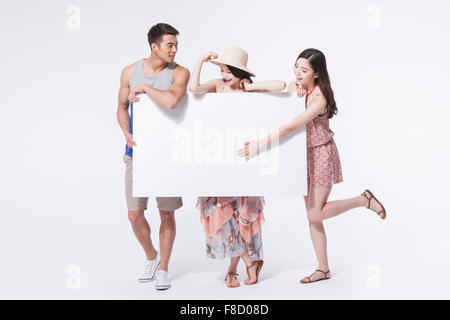 Two women and a man in tourist style of fashion standing and holding a white copy space with a hand of woman's pointing on the Stock Photo