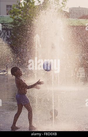 kid playing with a ball in a sunny water fountain Stock Photo