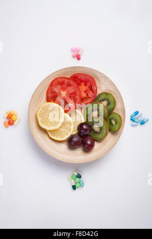 High angle of colorful vitamin pills around a plate with different color of vegetable slices and fruit slices Stock Photo