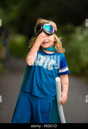 A small pre-teen boy in a home made costume and goggles  dressed up and playing outdoors at being Mini Superhero  on a summer evening , UK Stock Photo