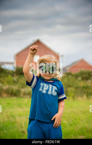 A small pre-teen boy in a home made costume and goggles  dressed up and playing outdoors at being Mini Superhero  on a summer evening , UK Stock Photo