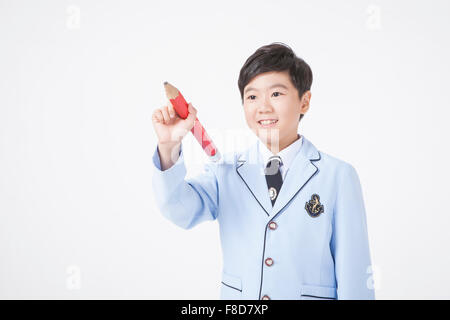 Elementary school age boy holding a big red pencil in his hand with gesture of writing Stock Photo
