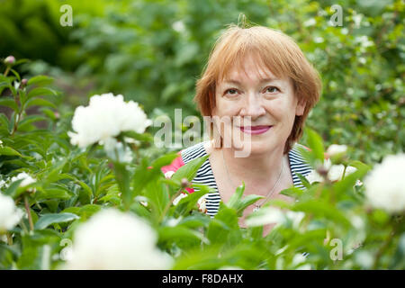 Happy mature woman in yard gardening with peony plant Stock Photo