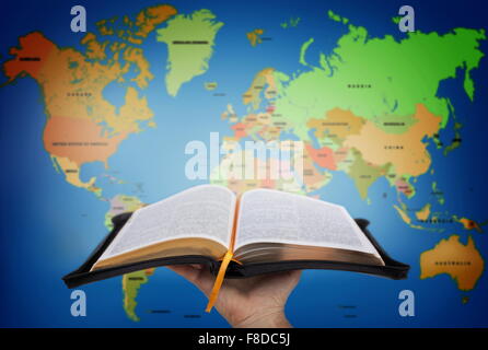 Hand showing the Holy Bible against world map Stock Photo