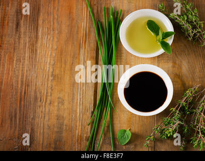 Olive oil, balsamic vinegar and herbs on a vintage wooden background from above. Stock Photo