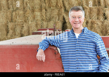Farmer Standing In Front Of Bales And Old Farm Equipment Stock Photo