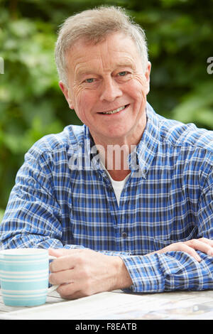 Senior Man Relaxing In Garden With Drink And Newspaper Stock Photo