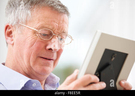 Unhappy Senior Man Looking At Photo In Frame Stock Photo