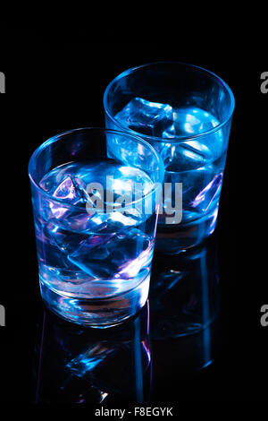 Two glasses with vodka and ice cubes against the background of deep blue glow on  dark mirror Stock Photo