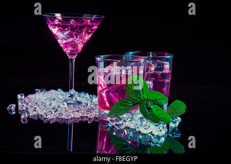 wine glass and two glasses with pink martinis, fine fragments of ice, fresh mint on  a dark mirror background Stock Photo