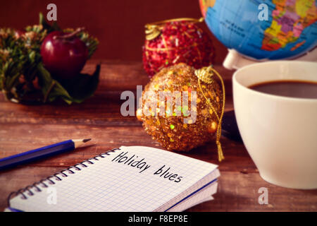 closeup of a notebook with the text holiday blues written in it on a rustic wooden table with some christmas ornaments, a cup of Stock Photo