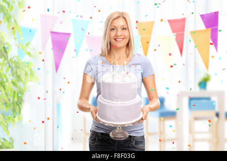 Cheerful young woman holding a birthday cake and looking at the camera at homed Stock Photo
