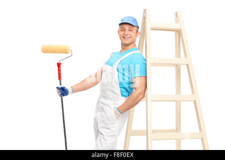 Young male decorator holding a paint roller and leaning on a wooden ladder isolated on white background Stock Photo