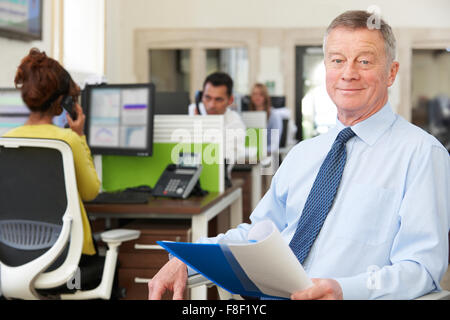 Portrait Of Senior Businessman Sitting In Busy Modern Office Stock Photo