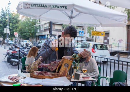 Man cutting Spanish serrano cured ham from the bone of a ham on the streets outside a bar in Granada in Spain Stock Photo