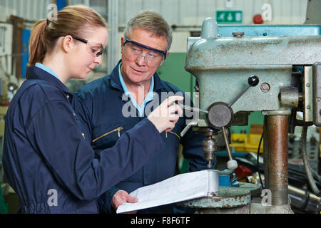 Engineer Showing Female Apprentice How To Use Drill In Factory Stock Photo