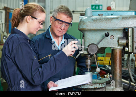 Engineer Showing Female Apprentice How To Use Drill In Factory Stock Photo