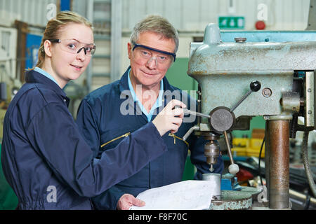 Engineer Showing Female Apprentice How To Use Drill In Factory Stock Photo