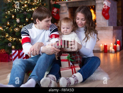 Happy family with gifts sitting at Christmas tree near fireplace Stock Photo