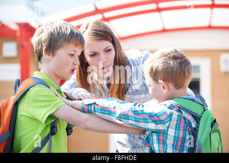 Teacher Stopping Two Boys Fighting In Playground Stock Photo