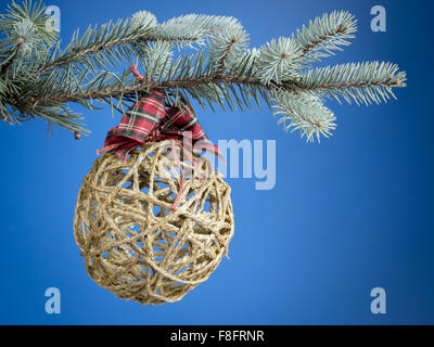 Christmas ball formed from hemp string hanging on spruce branch over blue background Stock Photo