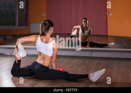 Full Length Rear View of Young Brunette Woman Stretching Legs in Splits Position and Looking at Reflection of Self in Mirrors in Dance Studio. Stock Photo