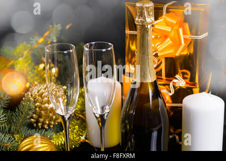 Sparkling Festive Still Life - Antique Pocket Watch Hanging from Neck of Champagne Bottle Surrounded by Elegant Glasses, White Pillar Candles, Gold Wrapped Gifts and Festive Evergreens. Stock Photo