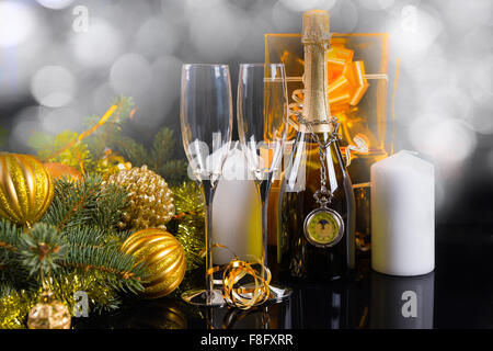 Sparkling Festive Still Life - Antique Pocket Watch Hanging from Neck of Champagne Bottle Surrounded by Elegant Glasses, White Pillar Candles, Gold Wrapped Gifts and Festive Evergreens. Stock Photo