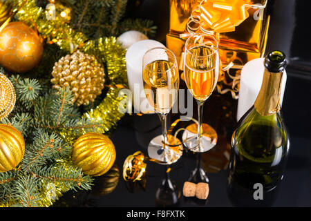 High Angle Festive Still Life - Two Glasses of Sparkling Champagne with Bottle, Candles, Gifts and Christmas Decorations on Black Background. Stock Photo