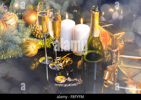 High Angle Festive Still Life - Two Glasses of Sparkling Champagne with Bottle, Candles, Gifts, Pocket Watch and Christmas Decorations on Black Background with Shimmering Effect. Stock Photo