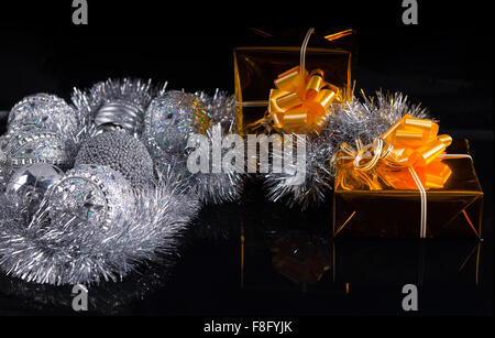 Festive Christmas still life with silver decorations and tinsel and two luxury gold gifts decorated with bows on a dark background with copyspace. Stock Photo